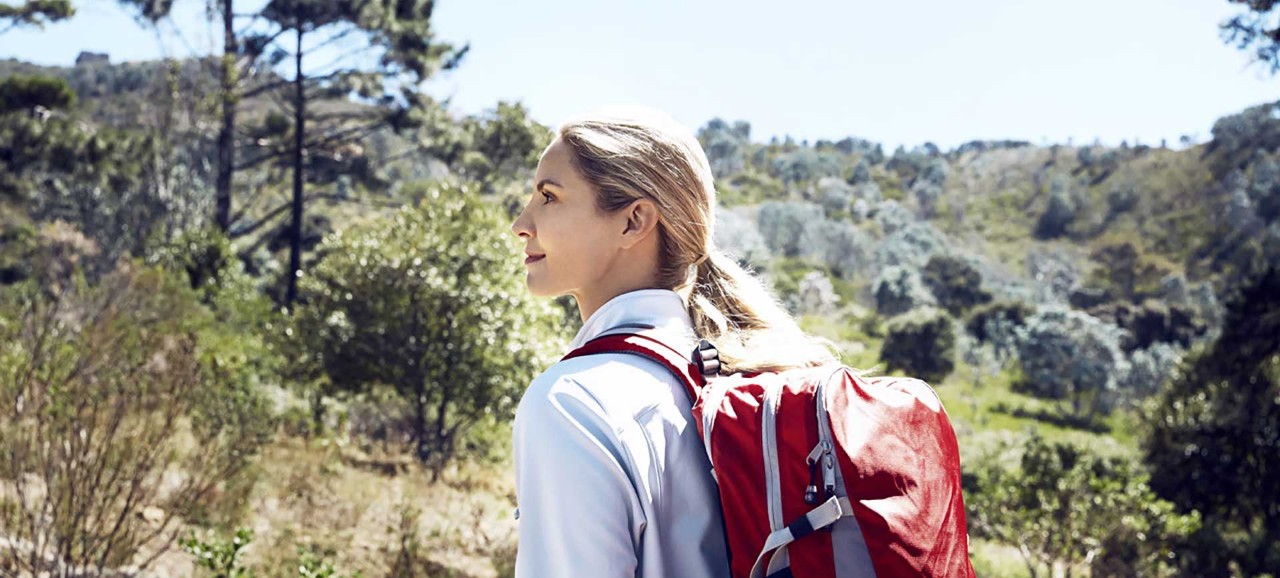 A young woman walking through trees with a red backpack